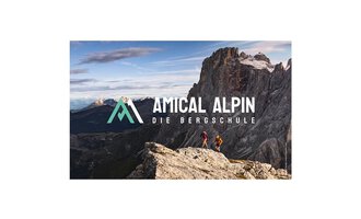 Zwei Personen wandern auf einem Felsen mit Blick auf beeindruckende Berge. Der Logo von "Amical Alpin" ist prominent im Bild platziert. | © SALEWA | Fotograf Storvteller Labs