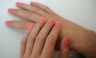 Zwei Hände mit einem leuchtend neonpinken Nagellack sind übereinandergelegt. Der Hintergrund ist hell und neutral. | © Annett Schwärzler Nails & Spa | Stefanie Haid