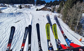 © Austrian Ski- & Service Ranch | Trixi Leitner Eine verschneite Skipiste mit Bäumen und Hütten im Hintergrund. Skier sind im Vordergrund zu sehen. | © Austrian Ski- & Service Ranch | Trixi Leitner