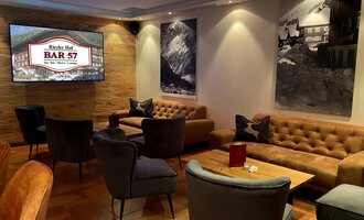 © Hotel Riezler Hof | M. Hasterok Eine elegante Bar mit bequemen Sitzgelegenheiten und warmen Holztönen. An den Wänden hängen schöne Schwarz-Weiß-Fotografien. | © Hotel Riezler Hof | M. Hasterok