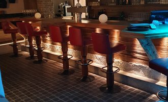 © Hotel Steinbock Eine gemütliche Bar mit roten Hochstühlen und einer Holztheke. Der Raum ist sanft beleuchtet und sorgt für eine entspannte Atmosphäre. | © Hotel Steinbock