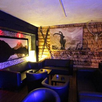 A cozy interior with dark leather furniture and wooden paneling. On the wall hangs a picture of a mountain panorama and a stylized goat motif. | © Heiko Möller m&m bar