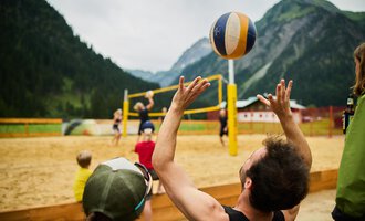 Ein Sandvolleyballspiel in den Bergen. Spieler werfen den Ball in die Luft, während andere zuschauen. | © Kleinwalsertal Tourismus | Oliver Farys