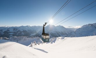 A mountain cable car glides over a snow-covered landscape. In the background, majestic mountains stretch under a clear blue sky. | © OBERSTDORF · KLEINWALSERTAL BERGBAHNEN