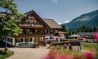Ein gemütlicher Gasthof mit einem schönen Café und Blick auf die Berge. Umgeben von grünen Wiesen und einem klaren blauen Himmel.