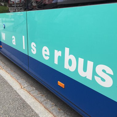A public bus with the inscription "walserbus" in light blue and blue color. The bus is at a stop on a street. | © Kleinwalsertal Tourismus