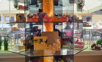 © Kleinwalsertal Tourismus | N. Lughammer An elegant showcase with various artistically decorated cakes and treats. Flowers and decorative elements add an appealing atmosphere to the overall picture. | © Kleinwalsertal Tourismus | N. Lughammer