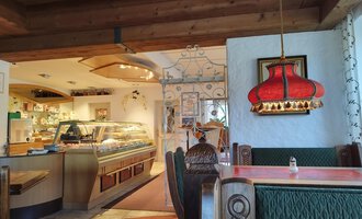 © Kleinwalsertal Tourismus | N. Lughammer A cozy restaurant with wooden furniture and a warm atmosphere. In the background, there is a bar and a striking red lamp visible. | © Kleinwalsertal Tourismus | N. Lughammer