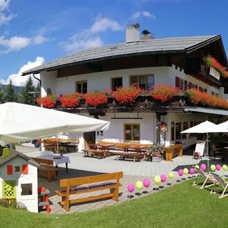 Ein charmantes Alpenhaus mit blühenden Balkonkästen und einer einladenden Terrasse. Die Umgebung ist grün und die Aussicht auf die Berge ist atemberaubend. | © Cafe Walserblick | Marcus Dornach