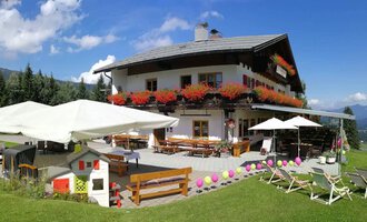 Ein charmantes Alpenhaus mit blühenden Balkonkästen und einer einladenden Terrasse. Die Umgebung ist grün und die Aussicht auf die Berge ist atemberaubend. | © Cafe Walserblick | Marcus Dornach