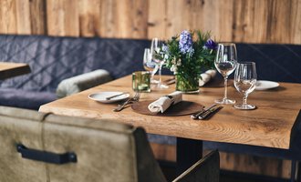A beautifully set table in a cozy restaurant. The wooden surface is decorated with glasses, dishes, and a flower. | © Travel Charme Ifen Hotel