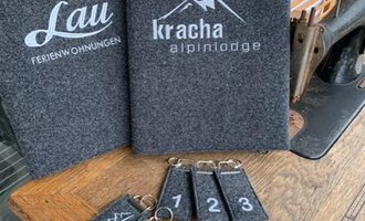 © Chrömle Schönes aus Filz | Anke Drechsel A wooden tray with keychains and two menus in a rustic setting. The tags are numbered and feature mountain motifs. | © Chrömle Schönes aus Filz | Anke Drechsel