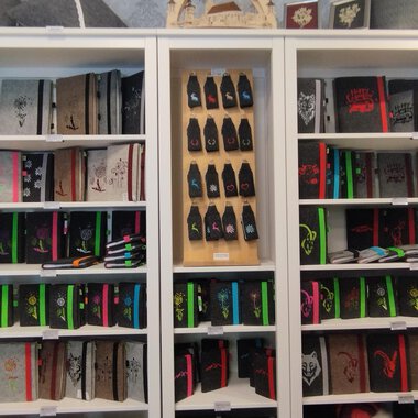 A bookshelf with many notebooks in various colors and designs. Below are colored pens and other stationery. | © Chrömle Schönes aus Filz | N. Lughammer