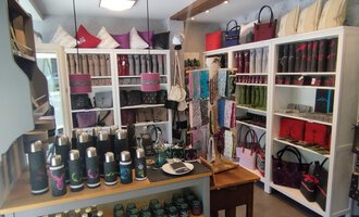 © Chrömle Schönes aus Filz | N. Lughammer Ein stilvoller Laden mit Regalen, die verschiedene Taschen und Accessoires ausstellen. Auf einem Tisch im Vordergrund sind diverse Trinkflaschen und Produkte angeordnet. | © Chrömle Schönes aus Filz | N. Lughammer