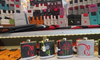 © Chrömle Schönes aus Filz | N. Lughammer Eine Auswahl an stilvollen Flaschen in verschiedenen Designs steht auf einem Regal. Im Hintergrund sind viele bunte Accessoires und Taschen zu sehen. | © Chrömle Schönes aus Filz | N. Lughammer