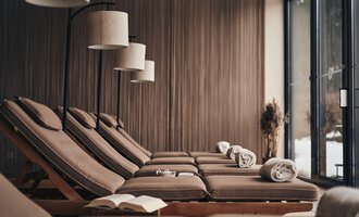 © Travel Charme Ifen Hotel Ein entspannender Wellnessbereich mit bequemen Liegen und sanfter Beleuchtung. Große Fenster bieten einen Blick auf die Natur. | © Travel Charme Ifen Hotel