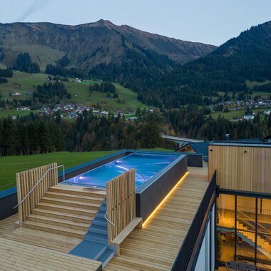 Eine moderne Terrasse mit einem Pool und Holzfußboden, umgeben von malerischen Bergen. Die Aussicht auf die Landschaft ist atemberaubend und vermittelt ein Gefühl von Ruhe. | © Genuss- & Aktivhotel Sonnenburg |Heike Wohlgenannt