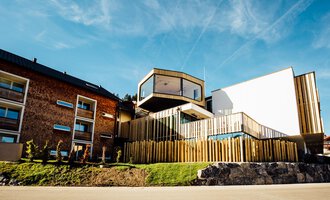 © Genuss- & Aktivhotel Sonnenburg |Heike Wohlgenannt Ein modernes Gebäude mit Holzverkleidung und klaren Linien. Es befindet sich in einer grünen Umgebung, umgeben von anderen Häusern. | © Genuss- & Aktivhotel Sonnenburg |Heike Wohlgenannt