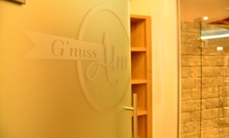 © Hotel Alpenstüble Appartements | Manuel Riezler Eine Tür mit dem Schriftzug „G'nuss Alm“ ist im Bild sichtbar. Der Bereich scheint einladend und modern gestaltet zu sein. | © Hotel Alpenstüble Appartements | Manuel Riezler