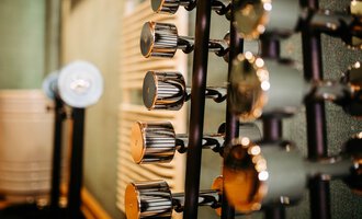 Eine Reihe von Hanteln in einem Fitnessstudio. Der Hintergrund ist unscharf und zeigt Texturen der Wände.