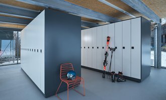 © Sport Kessler GmbH A modern ski room with white lockers and a red chair. Ski equipment and a helmet are on the wall. | © Sport Kessler GmbH