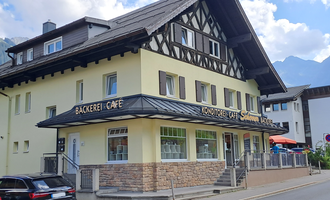 Ein hübsches Café mit einer Bäckerei in einem traditionellen Gebäude. Im Hintergrund sind Berge und ein blauer Himmel sichtbar. | © Kleinwalsertal Tourismus | Steffen Stöhr