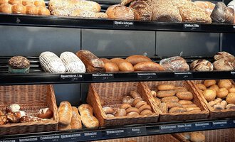 Eine Auswahl verschiedener Brotsorten in einer Bäckerei. Die Regale sind voll mit frischen Brötchen und Broten. | © Ehrat´s Backmanufaktur | Veronika Senn