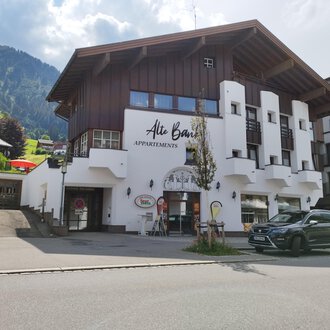 A modern building with a wooden and plaster facade that offers apartments. In the background, green mountains and a blue sky can be seen. | © Kleinwalsertal Tourismus | N. Lughammer