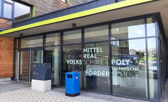A modern school building with large windows and an inviting entrance. The facade displays the names of various types of schools. | © Kleinwalsertal Tourismus | Veronika Senn
