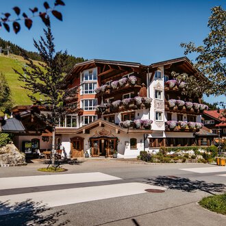 A picturesque hotel in alpine style with blooming balconies. Surrounded by green hills and a quiet road.