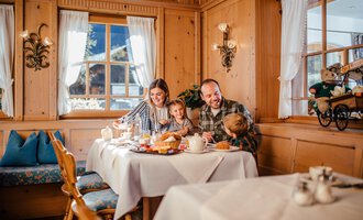 A family enjoys breakfast in a cozy wooden house. On the table are various breakfast dishes and a friendly atmosphere.