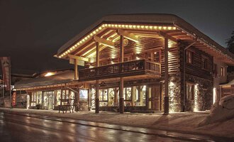 A cozy wooden building with warm light at night. The snow-covered ground and stylish design create an inviting atmosphere. | © Fun-Alp