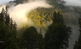 Eine beeindruckende Berglandschaft mit Nebel und Wolken. Die Sonne beleuchtet die grüne Vegetation in der Umgebung. | © Gasthof Café Alpenwald | Thorsten Alpenwald