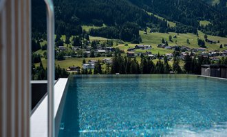 Ein infinity Pool mit glitzerndem Wasser und Blick auf grüne Hügel. Die umliegende Landschaft ist bergig und ruhig.