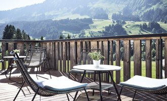 Eine Terrasse mit modernen Stühlen und Tischen. Im Hintergrund sind grüne Hügel und Berge zu sehen.