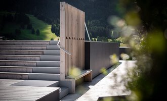 Eine moderne Terrasse mit einer Holzstruktur und sanften Stufen. Im Hintergrund sind grüne Hügel und Bäume zu sehen.
