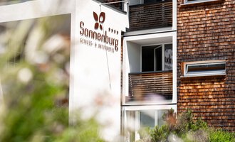 Ein modernes Gebäude mit dem Schriftzug "Sonnenburg". Umgeben von grüner Vegetation und blühenden Pflanzen.