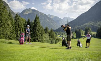 Eine Gruppe von Golfern übt auf einem malerischen Golfplatz mit Bergen im Hintergrund. Die Sonne scheint und die Landschaft ist grün und einladend. | © Golfclub Oberstdorf | ©kunst.joachimweiler.de