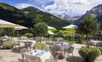 A stylish outdoor restaurant with a view of the mountains. There are elegant tables with umbrellas and green plants. | © Hallers Geniesserhotel | Dietmar Walser