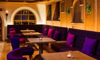 © Haller's Geniesserhotel | Dietmar Walser Ein einladendes Restaurant mit gemütlichen Sitzecken und warmem Holzinterieur. Die lila Kissen auf den Bänken schaffen eine entspannte Atmosphäre. | © Haller's Geniesserhotel | Dietmar Walser