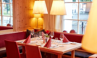 Ein einladendes Restaurant mit Holzdekoration und gemütlicher Atmosphäre. Der Tisch ist elegant gedeckt und mit roten Servietten dekoriert. | © Hotel Riezler Hof | M. Hasterok
