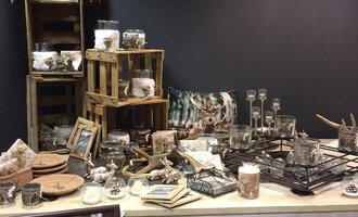 A stylish table with wooden decor and various glass containers. Picture frames and small natural accessories are also arranged on the table. | © HUIMWEA Alpendekor