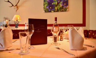 A beautifully set table in an elegant restaurant. On the table are glasses, a wine bottle, and a menu. | © IFA Breitach Apartements