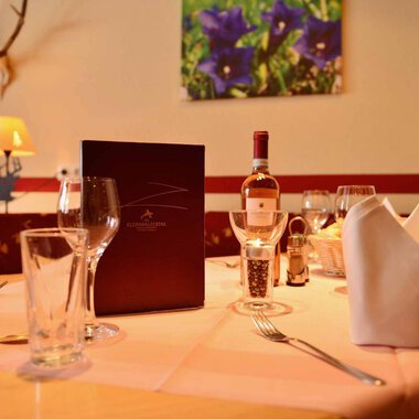 Ein schön gedeckter Tisch in einem eleganten Restaurant. Auf dem Tisch stehen Gläser, ein Weinflasche und eine Menükarte. | © IFA Breitach Apartements