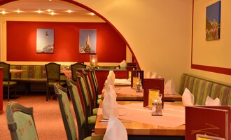 An elegant restaurant with tastefully decorated tables. The walls are in warm colors and adorned with pictures. | © IFA Breitach Apartements