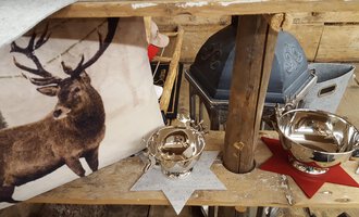 A rustic decoration with a cushion featuring an image of a deer, and shiny metal bowls. The bowls are positioned on red and gray stars on a wooden table.