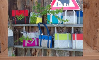 A selection of colorful bags hangs on a wooden shelf. In the background, there is a sign with a cow.