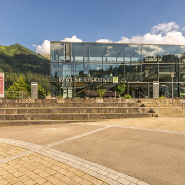 A modern building called Walserhaus in a mountainous environment. Surrounded by trees and under a clear sky. | © Kleinwalsertal Tourismus | Steffen Berschin