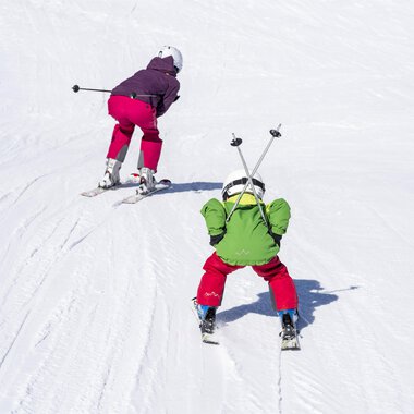 Zwei Kinder skifahren auf einer schneebedeckten Piste. Der Hintergrund ist hell und einladend. | © Kleinwalsertal Tourismus | Dominik Berchtold