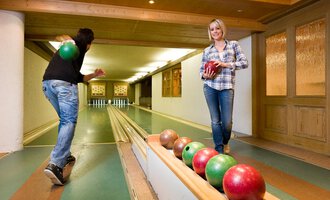 Eine gemütliche Kegelbahn mit zwei Personen, die spielen. Eine Person wirft eine Kugel, während die andere auf der Bahn steht und eine Kugel in der Hand hält. | © Aparthotel Kleinwalsertal Haller GmbH & Co KG